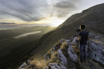 Rear view of man photographing while standing on mountain against sky