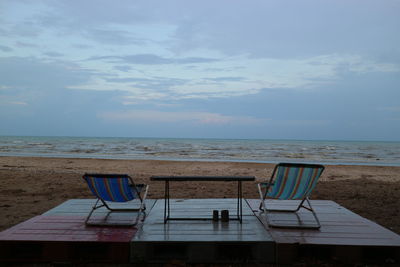 Chairs and table at beach against sky