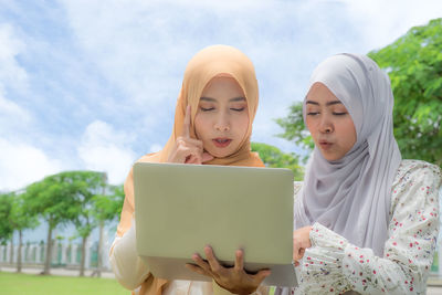 Woman using laptop while standing against sky