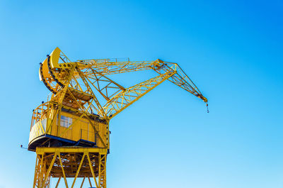 Low angle view of yellow crane against clear blue sky on sunny day