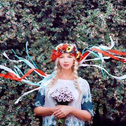 Portrait of beautiful young woman wearing flowers while standing against plants