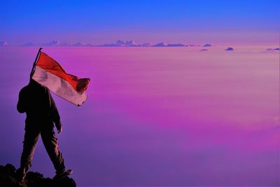 Man with pink umbrella against sky during sunset