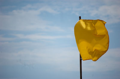 Low angle view of yellow flag waving against cloudy sky