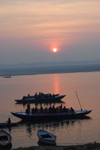 Boats moored in sea against sky during sunset