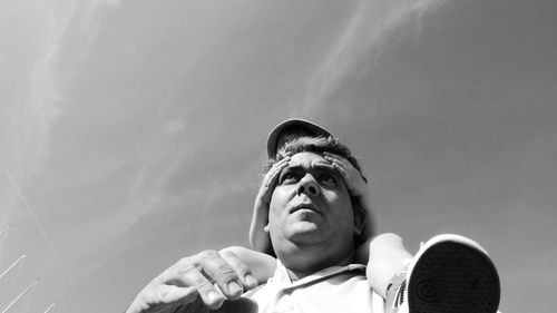 Low angle view of father carrying daughter on shoulder against sky