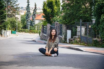 Portrait of woman sitting on road against trees in city