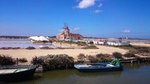 Sicily, saline marsala.  boats moored on canal by buildings against blue sky