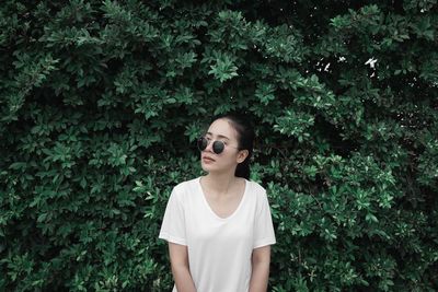 Young woman wearing sunglasses standing against plants