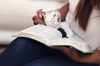 Young woman having coffee while reading book at home