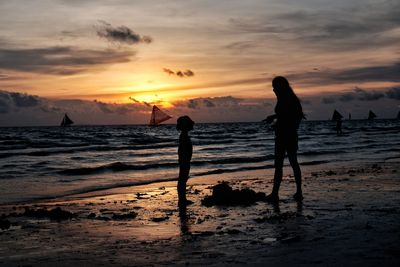Silhouette people standing on beach against sky during sunset