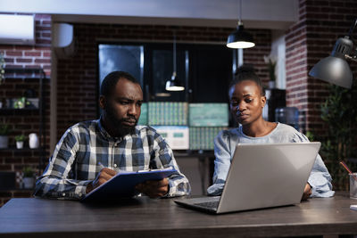 Male and female colleague using laptop at table