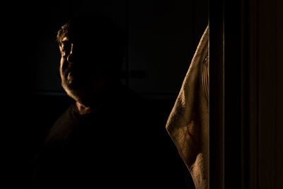 Side view of young man looking away against black background