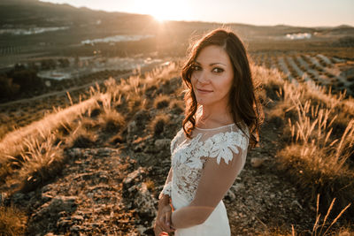 Portrait of young woman standing on field against sky during sunset