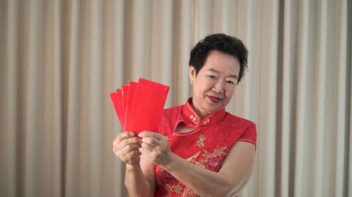 Portrait of smiling young woman holding red while standing against curtain