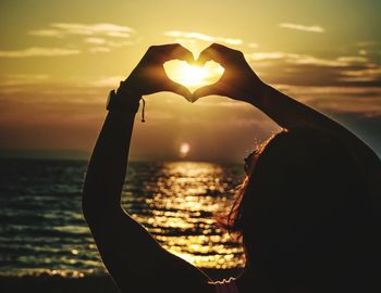 Silhouette man making heart shape against sky during sunset