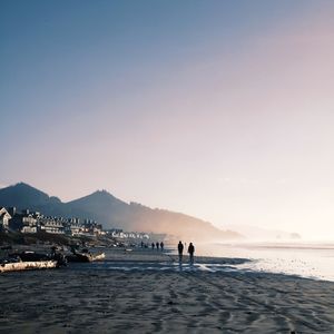 People on beach against clear sky during sunset