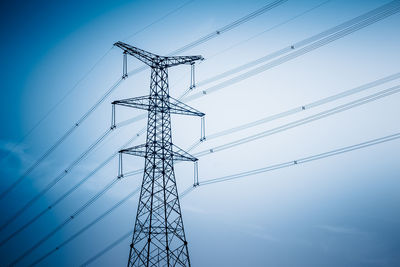 Low angle view of electricity pylon against clear blue sky