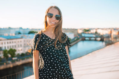 Portrait of woman wearing sunglasses standing against bridge