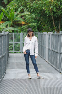 Full length of woman standing on railing against trees