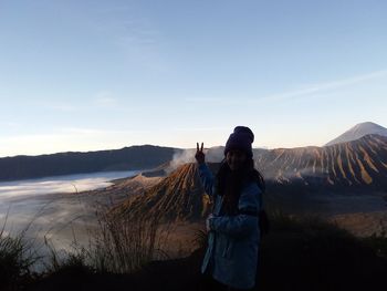 Woman gesturing peace sign while standing on volcanic landscape against sky