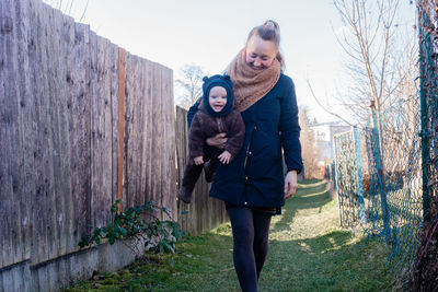 Smiling woman holding happy baby in her hands and against wooden wall. mother and son.