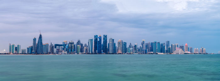 Sea by modern buildings in city against sky