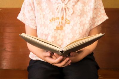 Midsection of woman holding book while sitting on seat