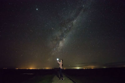 Side view of woman holding light while standing against star field