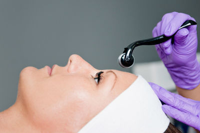 Close-up of woman lying down with while beautician using cosmetic roller on face at spa