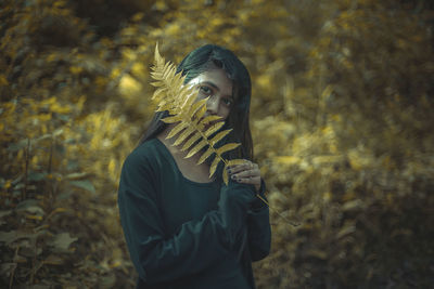 Portrait of young woman standing by tree in forest