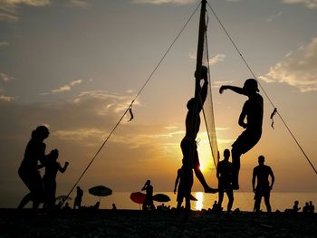 Silhouette friends playing volleyball at beach against sky during sunset