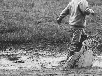 Low section of boy splashing water in puddle on field