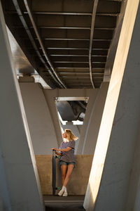 Relaxed female of middle age enjoy last summer sunset standing under urban bridge with longboard