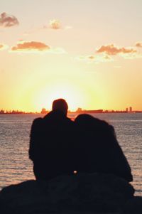 Rear view of lovers sitting on rock at sunset