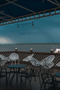 Empty chairs and tables in restaurant by sea against sky