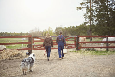 Rear view of mature couple walking towards gate in farm