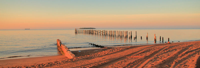 Remains of a wooden pier on beach against sky during sunset