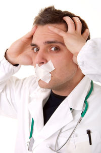 Close-up portrait of doctor with adhesive tape on mouth against white background