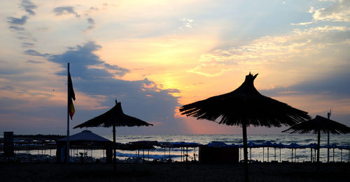 Silhouette parasols on beach against sky during sunset