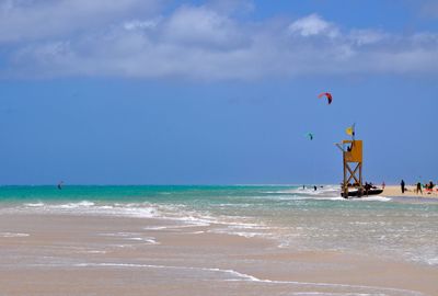 Tourists paragliding in sea during sunny day