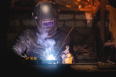 Village workshop, welding in an old garage. an unrecognizable man repairs a metal part wearing