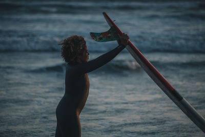 Woman carrying surfboard at sunset by pier