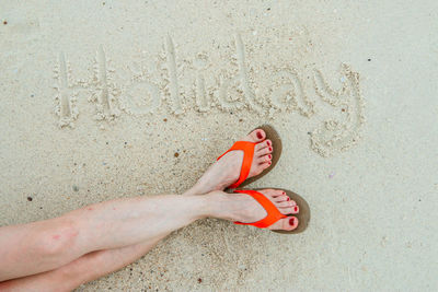 Low section of woman by holiday text on sand at beach