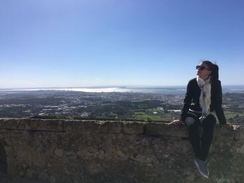 Young woman sitting on retaining wall against landscape