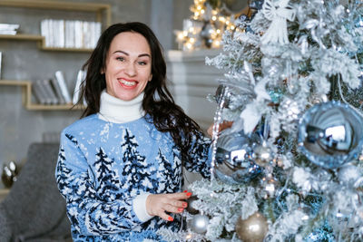 Portrait of young woman standing against christmas tree