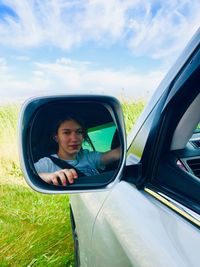 Reflection of teenage girl on side-view mirror against sky