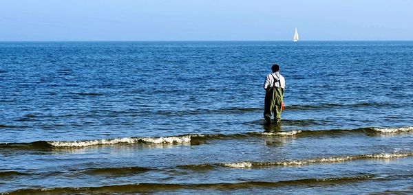 Rear view of man standing in sea against sky