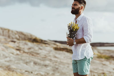 Man with flowering plant looking away while standing on land