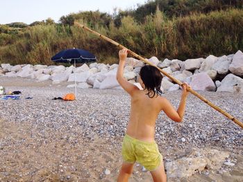 Rear view of shirtless boy throwing stick at beach