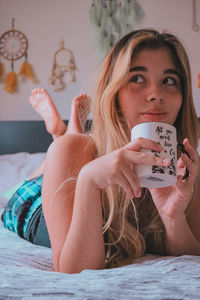 Portrait of young woman using mobile phone while relaxing on bed at home